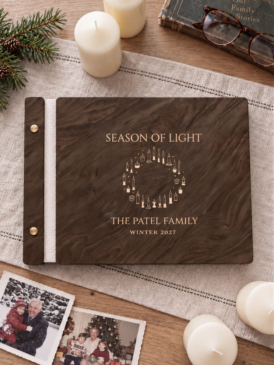 Jacobean wooden album with cream laser engraving of wreath formed by varied candles. The full personalized cover rests on a styled surface, with ivory binding and gold screws.
