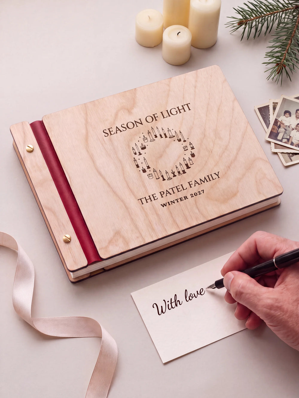 A Natural wooden album with the SEASON OF LIGHT engraving, cherry red binding and gold screws. A hand writes on a separate gift card beside the book.