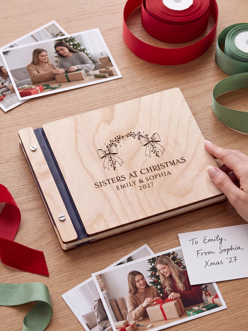 Natural wooden album with brown laser engraving of bow-tied evergreen arch, shown in a close lifestyle view with navy blue binding and silver screws. The cover reads SISTERS AT CHRISTMAS.