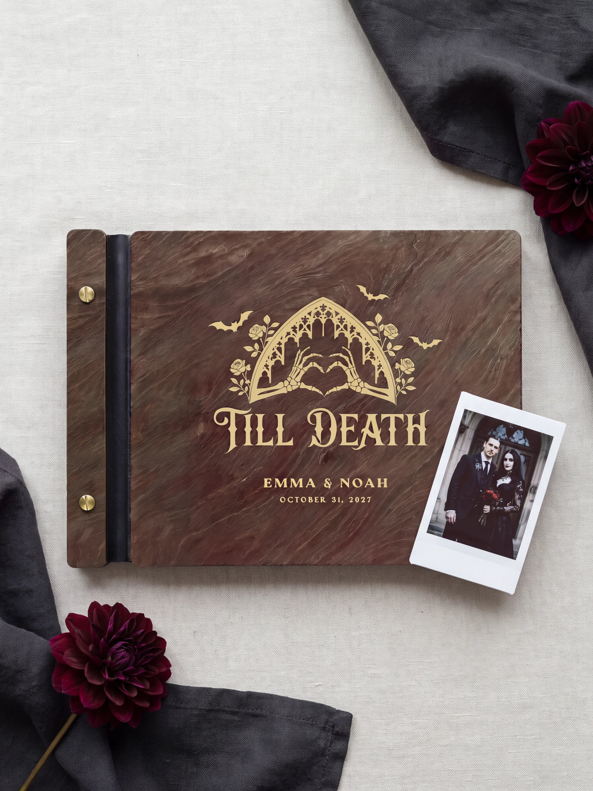 Jacobean wood Till Death wedding photo guest book lying flat on charcoal linen, the cover engraved with “TILL DEATH”, “EMMA & NOAH” and “OCTOBER 31, 2027”; two gold-tone screws along the black vegan leather spine