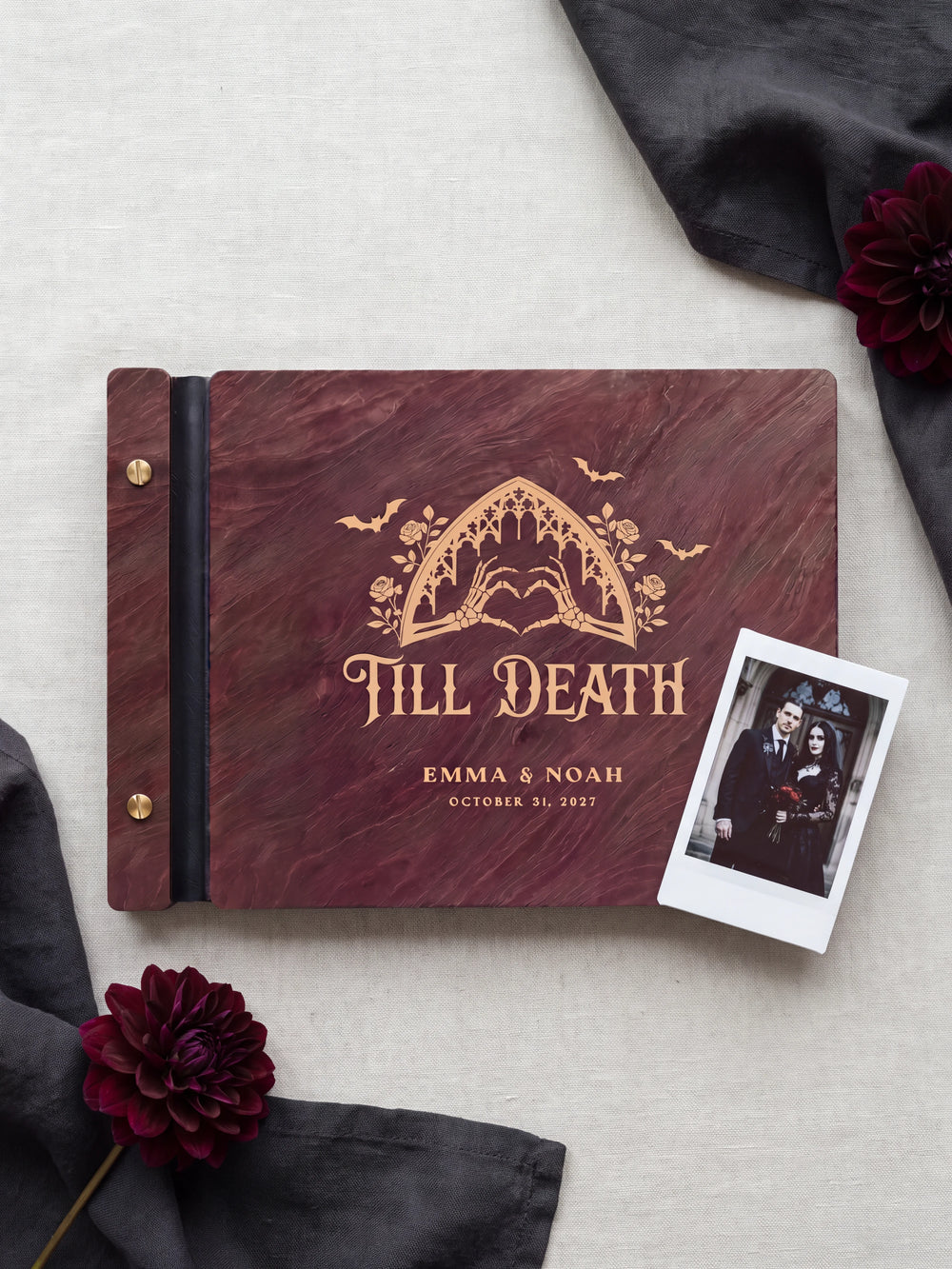 Jacobean wood Till Death wedding photo guest book lying flat on charcoal linen, the cover engraved with “TILL DEATH”, “EMMA & NOAH” and “OCTOBER 31, 2027”; two gold-tone screws along the black vegan leather spine