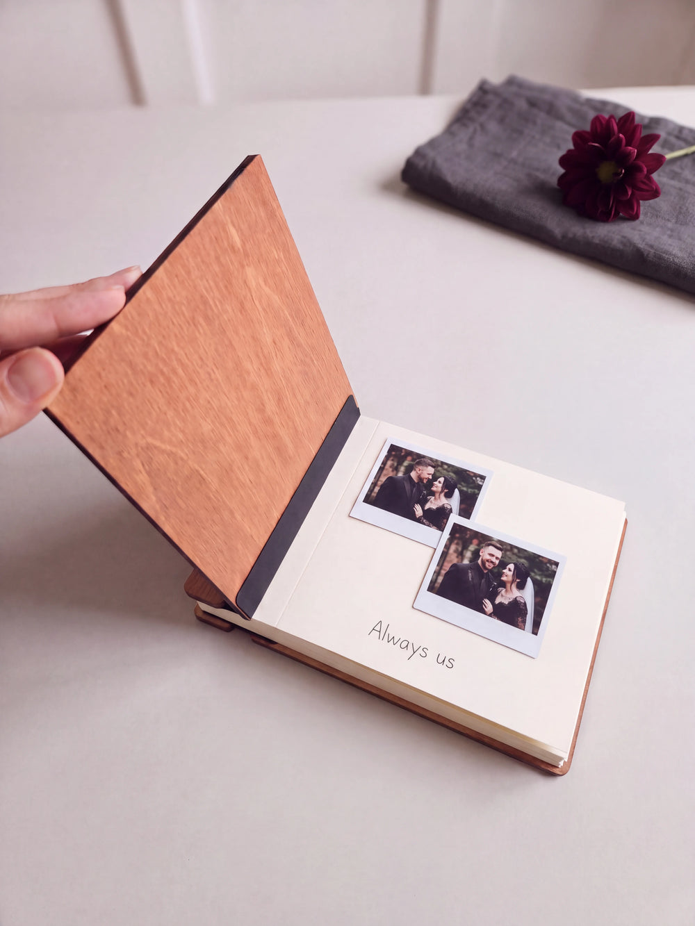 The Hazelnut Till Death wedding photo guest book open on a table with instant photos and a short handwritten note on a cream page; the black hinge strip is visible