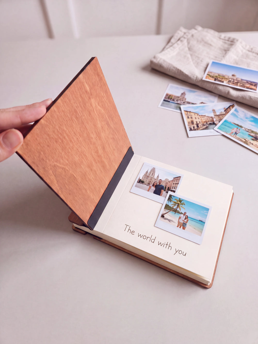 A hand lifts the Hazelnut album cover. Two couple vacation photos sit on a cream page above the handwritten note 