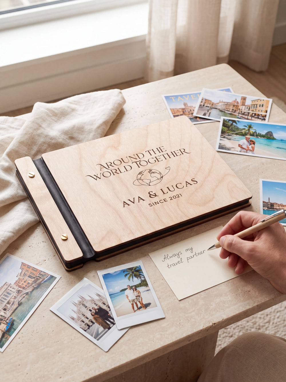 A Natural wooden album showing a globe with a looping travel path rests beside a separate gift card. A hand writes 