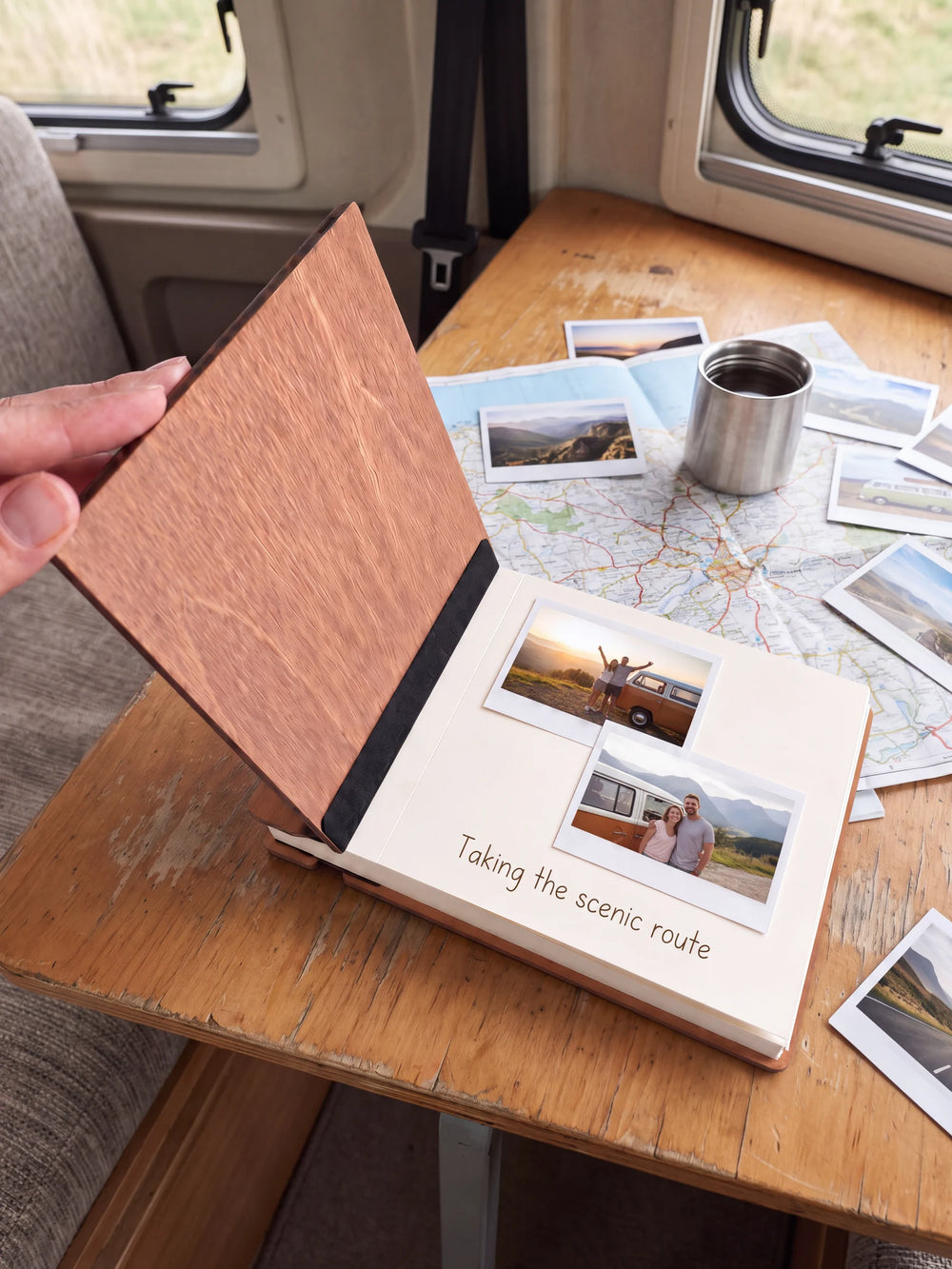 A hand lifts the Hazelnut album’s front cover, revealing a flat black inner fabric strip and a cream page arranged with instant photographs and a handwritten memory.