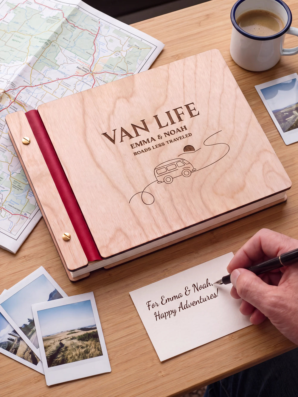 A Natural wooden album with the VAN LIFE engraving, cherry red binding and gold screws. A hand writes on a separate gift card beside the book.