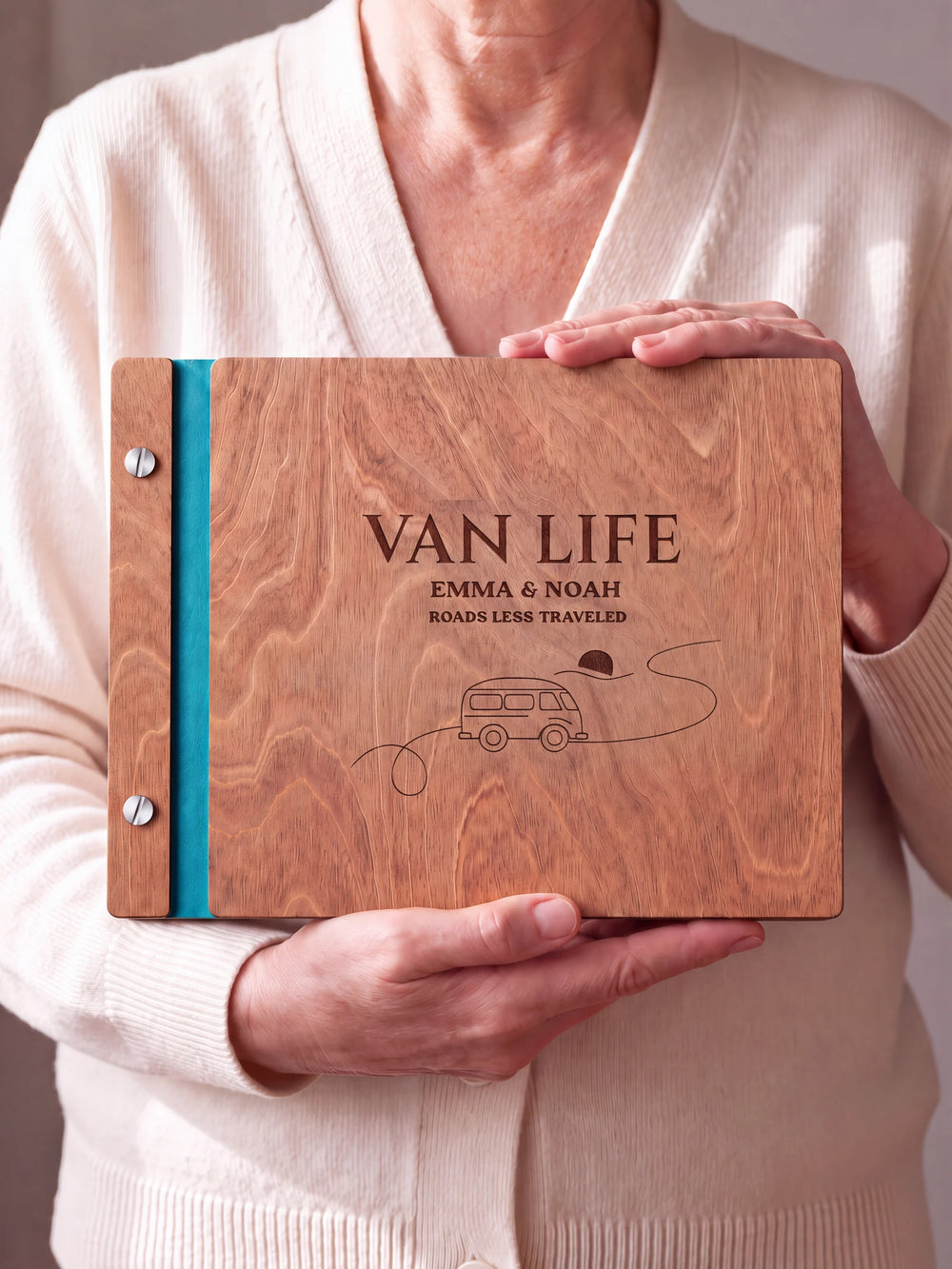 Two hands hold a Hazelnut wooden photo album. The VAN LIFE cover design has brown engraving, turquoise binding and silver screws.