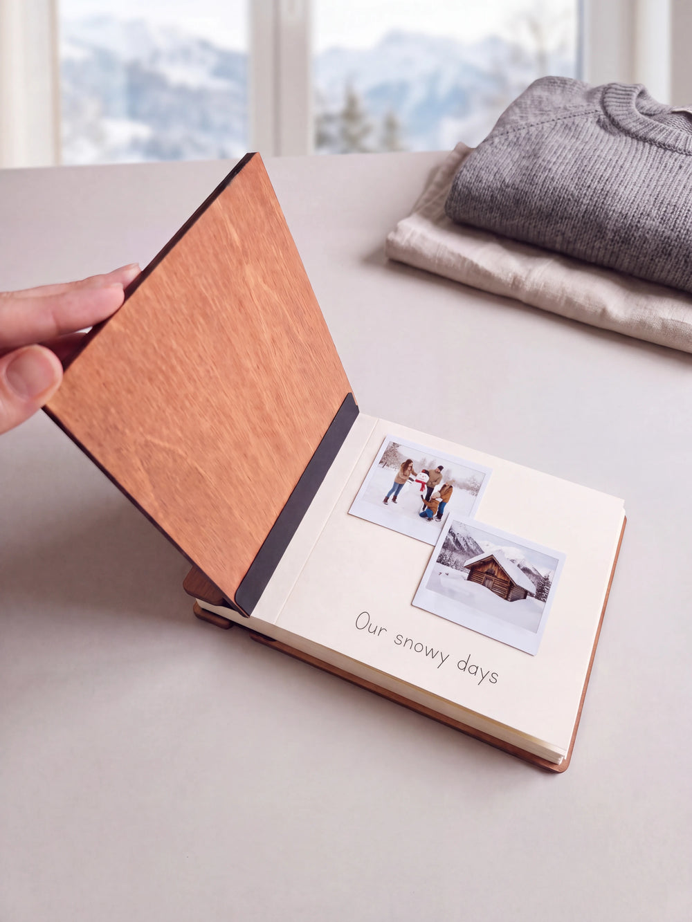 A hand lifts the Hazelnut album cover. Two family winter vacation photos sit on a cream page above the handwritten note 