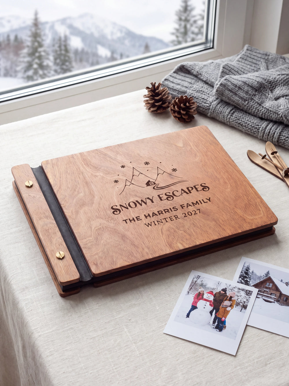 Hazelnut wooden album on a light tabletop with neutral linen. The full cover shows snowy mountains, a cabin and snowflakes, personalized wording and the two-screw binding.