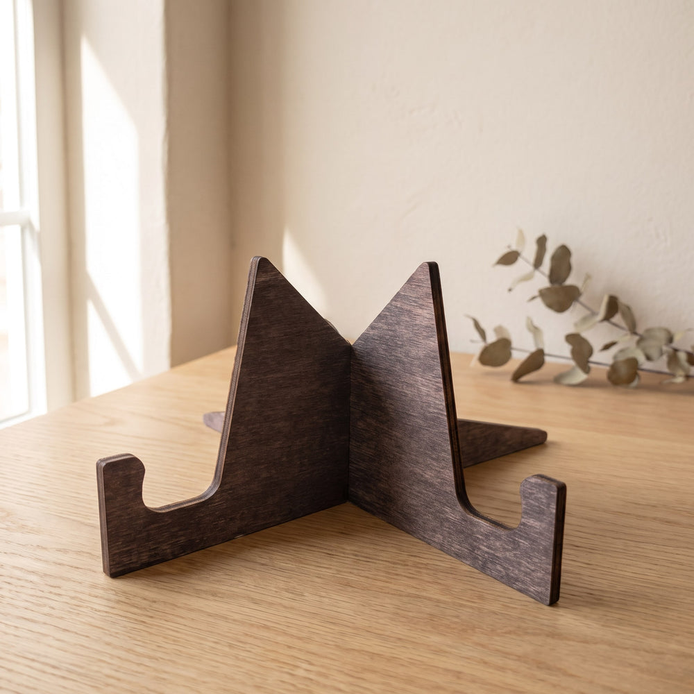 Wooden display stand for a round guest book sign, laser-cut Baltic birch in a dark stain, on an oak table